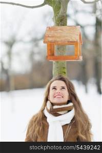 Happy young woman looking on bird feeder on tree in winter park