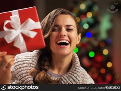 Happy young woman looking out from present box in front of christmas lights