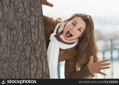 Happy young woman looking out from tree in winter park