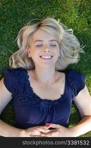 Happy young woman lying on grass with eyes closed