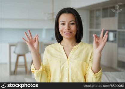 Happy young woman makes calmness mudra gesture, practice yoga, breathing out, calming down at home. Calm woman meditating, relaxing her mind, managing stress, keeping zen. Healthy lifestyle, wellness.. Female keeps calmness, makes mudra hand gesture, practice yoga at home. Stress relief, wellness