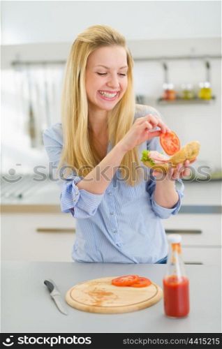 Happy young woman making sandwich in kitchen