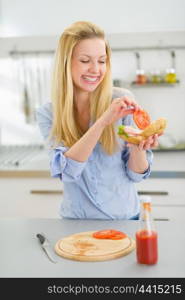 Happy young woman making sandwich in kitchen