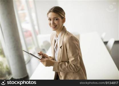 Happy young woman manager holding digital tablet and standing in modern office