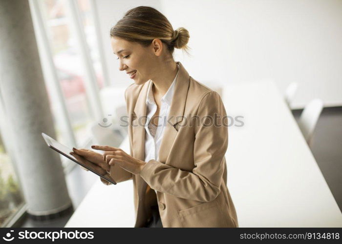 Happy young woman manager holding digital tablet and standing in modern office