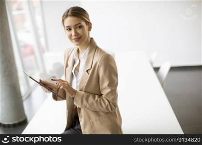 Happy young woman manager holding digital tablet and standing in modern office