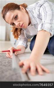 happy young woman measuring and marking laminate floor tile