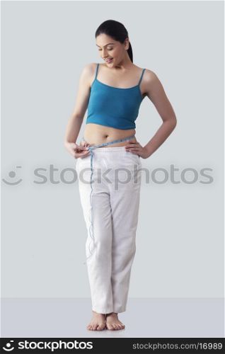 Happy young woman measuring waist against gray background