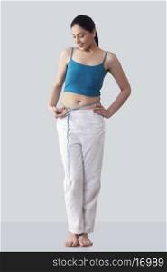 Happy young woman measuring waist against gray background