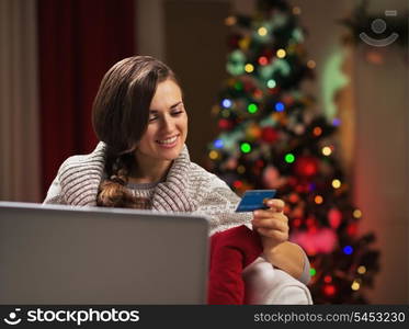 Happy young woman near christmas tree making online shopping