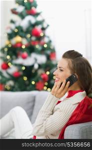 Happy young woman near Christmas tree making phone call