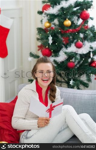 Happy young woman near Christmas tree reading postcard