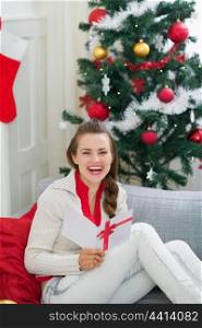 Happy young woman near Christmas tree reading postcard