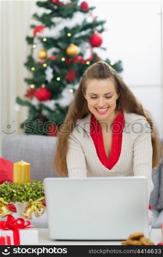 Happy young woman near Christmas tree using laptop