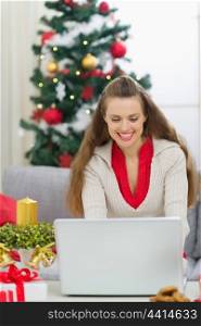 Happy young woman near Christmas tree using laptop