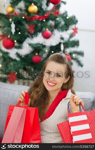 Happy young woman near Christmas tree with shopping bags