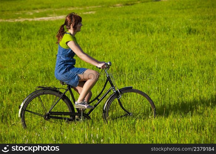 Happy young woman on a green meadow riding a bicycle