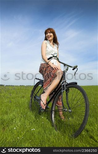 Happy young woman on a green meadow with a vintage bicycle