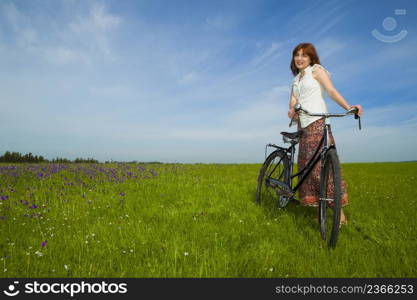 Happy young woman on a green meadow with a vintage bicycle