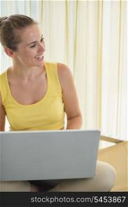 Happy young woman on chair with laptop looking on copy space