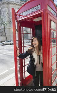 Happy young woman opening door of telephone booth at London; England; UK