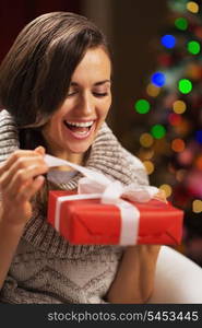 Happy young woman opening present box in front of christmas lights