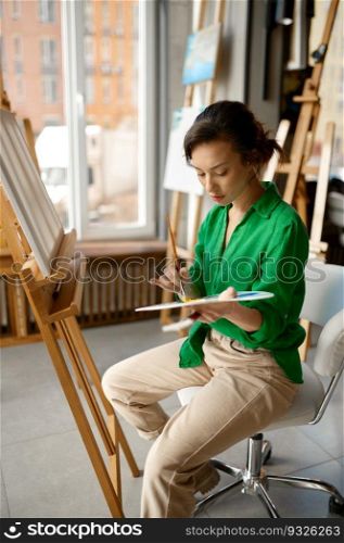 Happy young woman painting brush on canvas at workshop during art lesson class. Creative leisure activity concept. Woman painting brush on canvas at workshop during art lesson class
