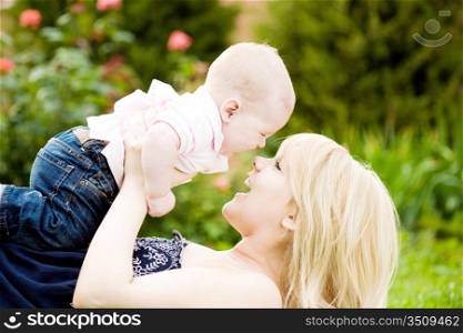 Happy young woman playing with baby boy in spring flowery garden. Nature blurred background