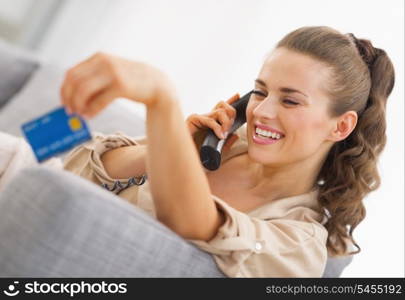 Happy young woman playing with credit card while talking phone