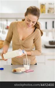 Happy young woman pouring milk into glass