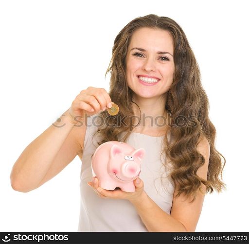 Happy young woman putting coin into piggy bank