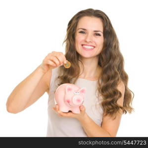 Happy young woman putting coin into piggy bank