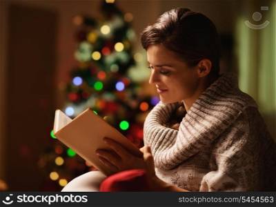 Happy young woman reading book in front of christmas tree