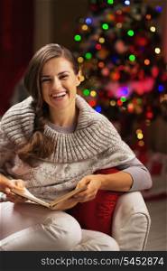 Happy young woman reading book near christmas tree