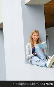 Happy young woman reading book outside of school smiling