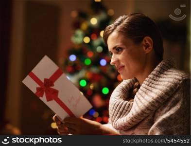 Happy young woman reading postcard in front of christmas tree