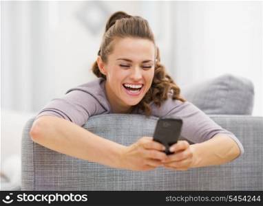 Happy young woman reading sms while laying on sofa