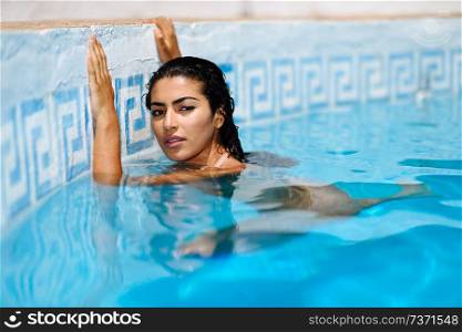 Happy young woman relaxing in swimming pool. Beautiful girl with healthy tanned skin and wet hair enjoying Summer Sun at pool edge.. Beautiful Arab woman relaxing in swimming pool.
