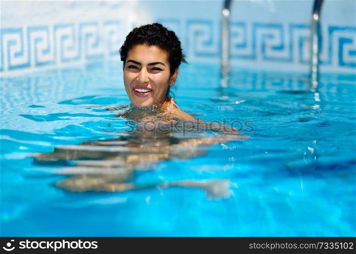 Happy young woman relaxing in swimming pool. Smiling girl with healthy tanned skin and wet hair enjoying Summer Sun at pool edge.. Happy young woman relaxing in swimming pool.