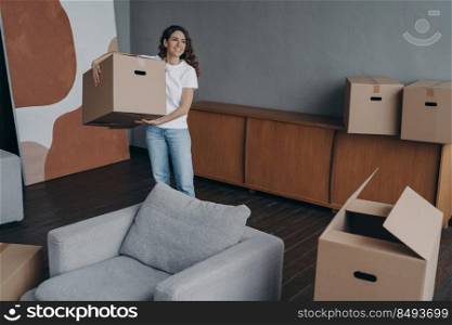 Happy young woman relocates alone and carrying a box. Single spanish lady moves. Apartment selling. Real estate purchase, mortgage, delivery service ordering concept.. Happy young woman relocates alone and carrying a box. Single spanish lady moves.