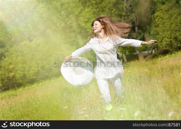 Happy Young Woman Running with a White Hat at the Green Meadow in the White Clothes.