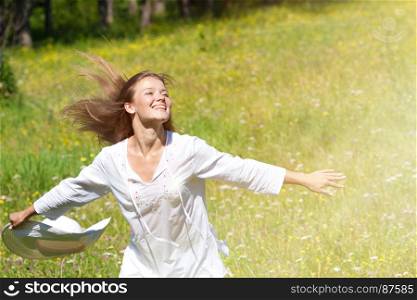 Happy Young Woman Running with a White Hat at the Green Meadow in White Clothes.