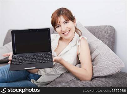 Happy young woman seated on sofa and showing something on the laptop