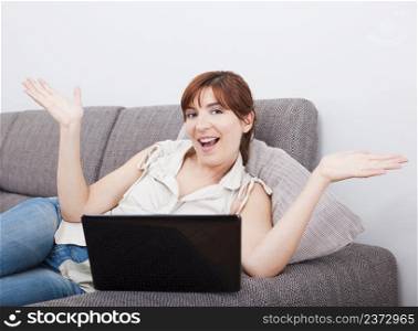 Happy young woman seated on sofa with a laptop