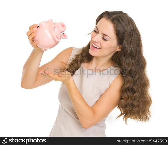 Happy young woman shaking out coins from piggy bank