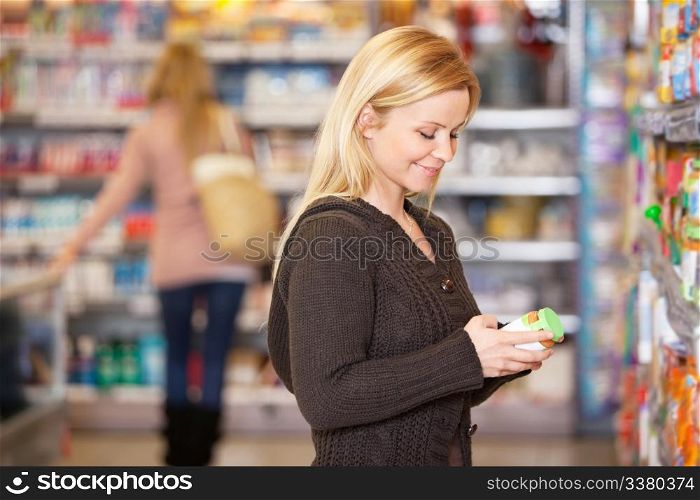 Happy young woman shopping in the supermarket with people in the background