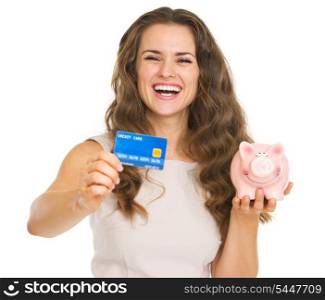Happy young woman showing credit card and piggy bank