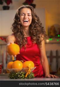 Happy young woman showing orange in christmas decorated kitchen