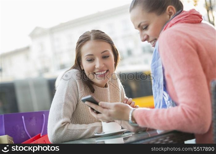 Happy young woman showing text message to friend at sidewalk cafe
