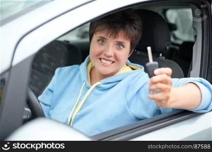 Happy Young Woman Showing the Key of Her New Car in her Hand in the Road. Selective Focus is on the Young Woman